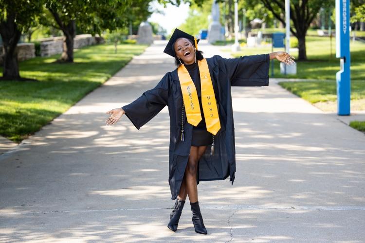 一个毕业生兴高采烈地站在大学的人行道上, 双臂伸展，头倾斜, 微笑